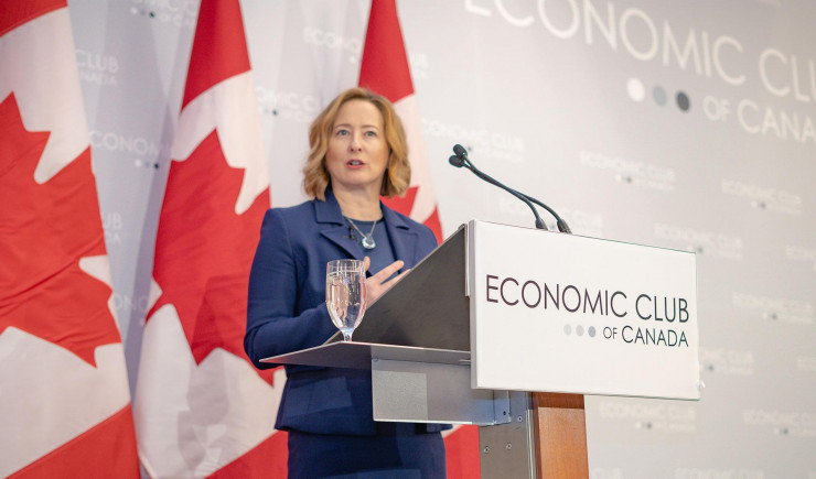 Carolyn Wilkins standing at a podium with Canadian flags behind her.