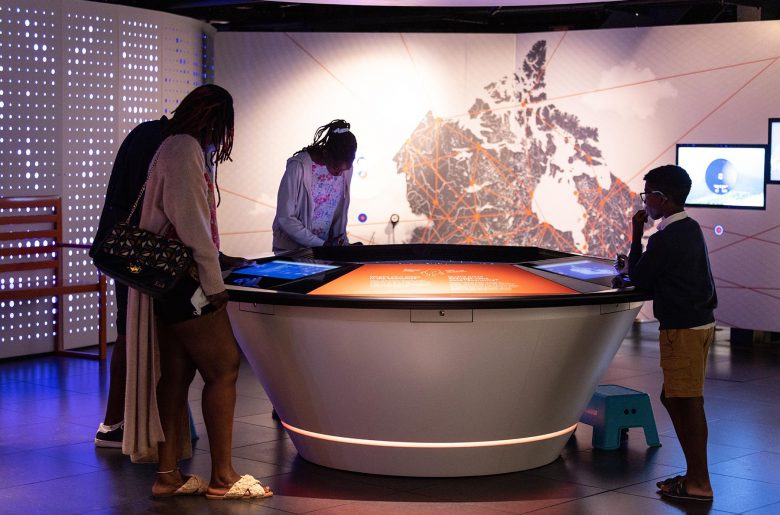 Four individuals interacting with a circular table with embedded digital pads in the Bank of Canada Museum.