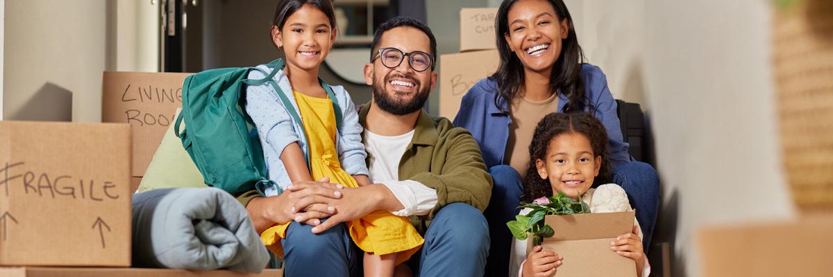 An immigrant family of four people is surrounded by moving boxes as they settle into new housing.