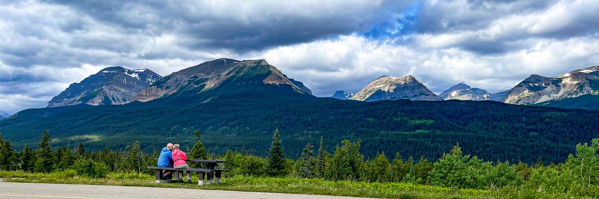 A older couple sitting on a bench admires a mountain view in western Canada.